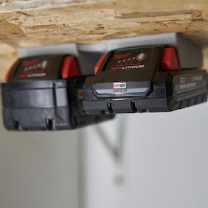 May include: Two black and red Milwaukee M18 CP3.0 REDLITHIUM high output batteries mounted on a gray wall mount.
