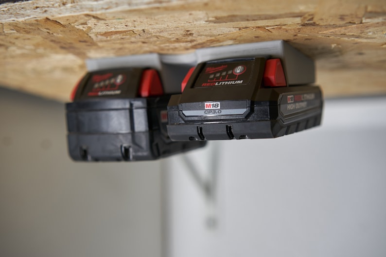 May include: Two black and red Milwaukee M18 CP3.0 REDLITHIUM high output batteries mounted on a gray wall mount.