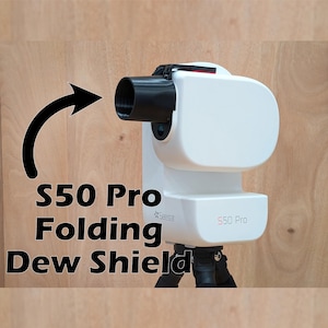 May include: A white S50 Pro telescope device featuring a black cylindrical folding dew shield attached to the front. The unit is mounted on a black tripod and displays the text S50 Pro on its side, with a black arrow pointing toward the shield.