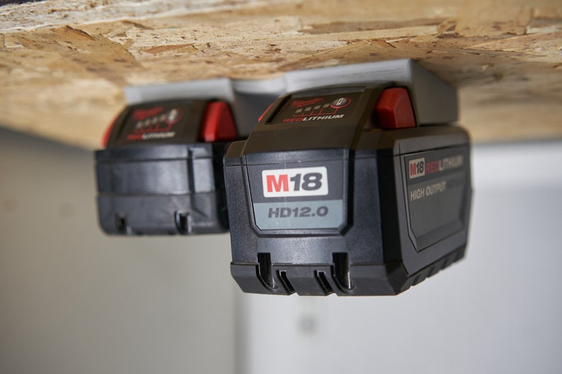 May include: Two black and red Milwaukee M18 HD12.0 high output lithium-ion batteries mounted on a wooden surface.