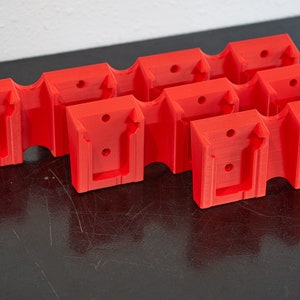 May include: Five red plastic wall mounts with a rectangular shape and a U-shaped cutout. The mounts have small holes for screws.