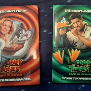 May include: Two red and green promotional buttons for the movie "Looney Tunes: Back in Action". The buttons feature Bugs Bunny and Daffy Duck with the text "The Bunny's Funny" and "The Duck's Amuck". The text "Looney Tunes: Back in Action" and "The Chase is on November 14, 2003" is also on the buttons.