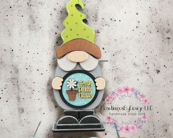 Può includere: Una collezione di 12 cartelli rotondi in legno con vari temi di vacanza e stagionali. I cartelli presentano disegni dipinti e testo, tra cui "Fresh Picked Daisies", "Freezin Season", "Back to School", "Hello Fall", "Trick or Treat" e "Give Thanks".