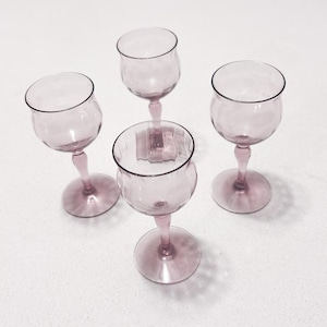 Puede incluir: Cuatro copas de vino vintage en un suave tono lavanda. Cada copa presenta un cuenco redondeado, un tallo delgado y una base circular. Las copas están dispuestas sobre una superficie blanca, mostrando su delicado diseño y color.