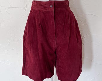 Puede incluir: Shorts de cintura alta color burdeos hechos de un material suave y aterciopelado. Los shorts tienen cierre de botón y pliegues en la cintura. Los shorts se muestran en un maniquí.