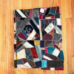 May include: A patchwork quilt with a variety of fabric pieces in shades of blue, red, green, and gold. The quilt has a hand-stitched design with the text "8. Om 1892" and a cat illustration.