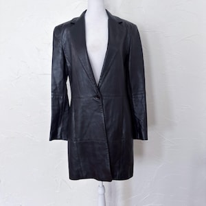 Può includere: Un blazer in pelle nera con chiusura a un bottone. Il blazer ha un classico risvolto e una vestibilità su misura, esposto su un manichino bianco. Il capo è uno stile cappotto lungo.