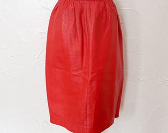 Könnte beinhalten: Ein leuchtend roter Lederrock. Der Rock hat eine klassische Bleistiftrock-Silhouette mit einer taillierten Taille und einem geraden, knielangen Saum. Das Leder hat ein leicht strukturiertes Aussehen, und der Rock wird auf einer Schaufensterpuppe präsentiert.