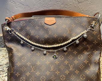 May include: A brown and tan monogrammed handbag with a pearl and silver chain with charms attached.