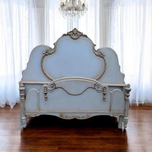 May include: A light blue, ornate bed frame with a high headboard and footboard. The bed features detailed carvings and a distressed finish, with cream-colored accents. The bed frame is a classic, elegant design.