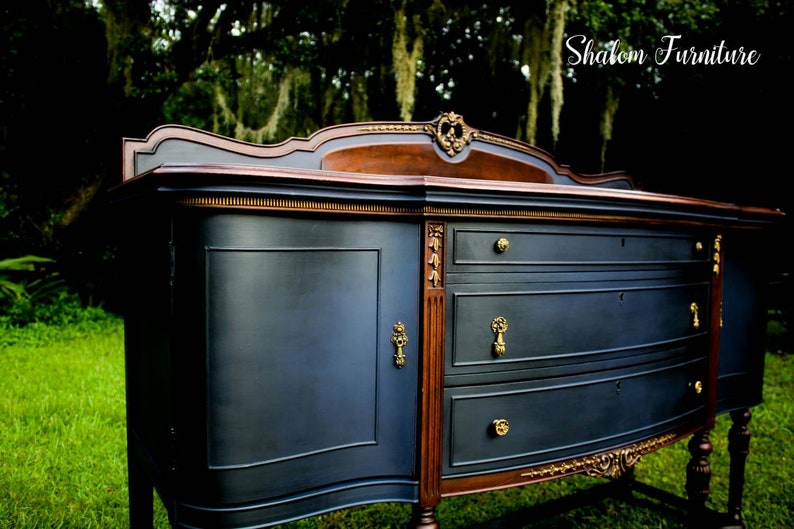 K&ouml;nnte beinhalten: Ein antiker Sideboard in Dunkelblau mit goldenen Akzenten und drei Schubladen. Das Sideboard hat eine geschwungene Front und verzierte Details. Die Oberseite des Sideboards ist aus dunklerem Holz.