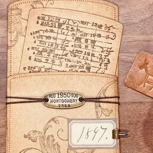May include: A vintage leather journal with a brass tag that reads "REO 1950 DOG MONTGOMERY 2569." The journal has a decorative floral design and a handwritten date of "1897."