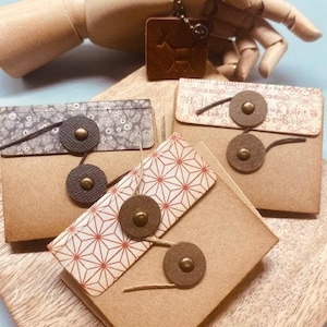May include: Three small, brown, rectangular journals with different patterned covers. The covers are decorated with geometric patterns and have metal accents. The journals are sitting on a wooden surface.