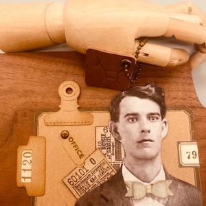 May include: A vintage-style collage featuring a man in a suit with a bow tie, a ticket with the text "60101 0", and a tag that says "OFFICE". The collage is on a wooden surface with a brown leather tag with a symbol.