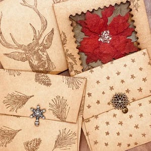 May include: Four brown paper envelopes with different holiday designs. One envelope features a deer, another a poinsettia, another pine branches, and the last one has a repeating star pattern. Each envelope has a snowflake-shaped metal embellishment.