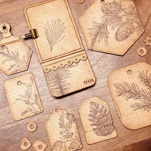 May include: A set of eight brown paper tags with various pine tree and holly designs. The tags are decorated with a scalloped edge and a stitched border.