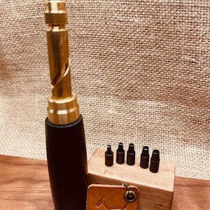 May include: A brass and black leather corkscrew with a set of black attachments and a small leather tag with a dog design. The corkscrew is approximately 7 inches tall.