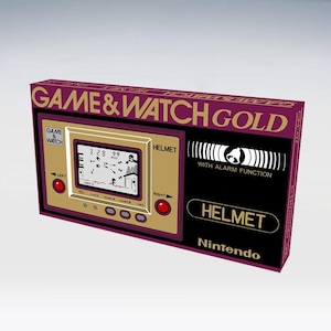 Può includere: Una console di gioco portatile Game & Watch Gold vintage. Il dispositivo presenta una combinazione di colori oro e bordeaux con il gioco "Helmet" visualizzato sullo schermo. La console ha il testo "GAME & WATCH GOLD" e "HELMET", e il logo Nintendo.