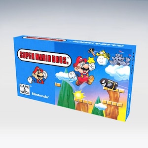 Puede incluir: Caja azul de Super Mario Bros. Game & Watch con Mario saltando sobre un paisaje con un castillo, nubes y un Bill Bala. La caja tiene el logotipo de Nintendo y el título del juego en un óvalo rojo y blanco.