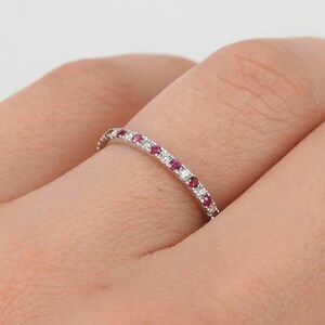 May include: A thin silver band ring with a row of small red and white gemstones.
