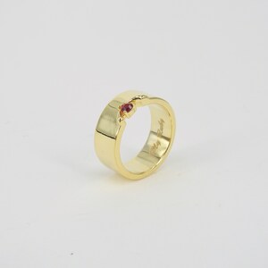 May include: A gold band ring with a small red gemstone set into the band. The inside of the band is engraved with the words "My Rudy".
