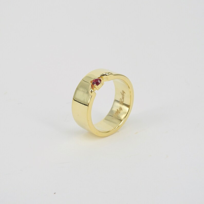 May include: A gold band ring with a small red gemstone set into the band. The inside of the band is engraved with the words "My Rudy".