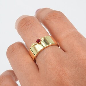 May include: A gold ring with a red gemstone set in a crown design.