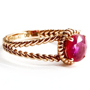 May include: A gold ring with a twisted band and a large, round, red ruby gemstone.