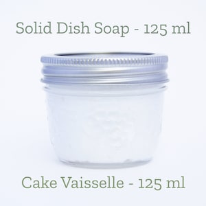 May include: A clear glass jar with a silver lid filled with white solid dish soap. The jar is labelled "Solid Dish Soap - 125 ml" and "Cake Vaissele - 125 ml".