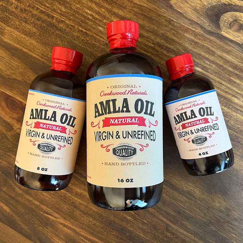 May include: Three glass bottles of Amla Oil, labeled "Original Creekwood Naturals Amla Oil Natural Virgin & Unrefined" with hand-bottled quality labels. The bottles are 4 oz, 8 oz, and 16 oz.