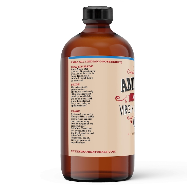 May include: A brown glass bottle of Amla Oil (Indian Gooseberry) with a white label. The label has the text "Amla Oil (Indian Gooseberry)", "How It's Made", "Pride", "Usage", and "Creekwoodnaturals.com".
