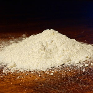 May include: A close-up of a pile of white flour on a brown wooden surface.
