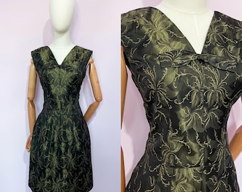 Può includere: Un abito vintage nero e verde oliva con motivo floreale. L'abito presenta uno scollo a V, un piccolo fiocco e un corpetto aderente che si allarga in una gonna al ginocchio. L'abito è esposto su un manichino.