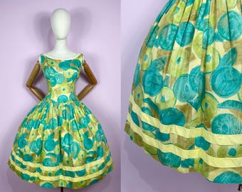 May include: A vintage dress with a vibrant pattern of teal and green circles on a yellow background. The dress features a fitted bodice, a flared skirt, and yellow trim. The dress is displayed on a mannequin.