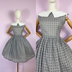 May include: A vintage dress featuring a white collar and a grey and black patterned design. The sleeveless dress has a fitted bodice and a full skirt. The dress is displayed on a mannequin, showcasing its classic silhouette.