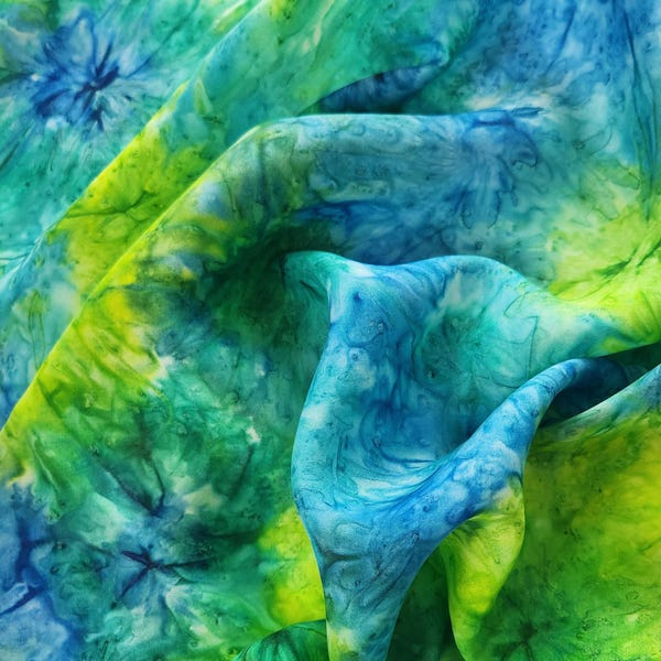 May include: A close-up of a blue and green fabric with a tie-dye pattern. The fabric is soft and flowing, with a subtle sheen.