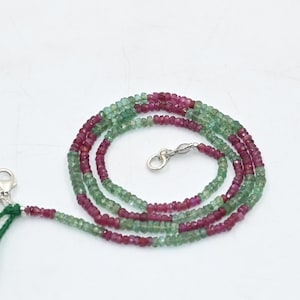 Könnte beinhalten: Eine Halskette aus grünen und rosafarbenen Edelsteinen mit einem silbernen Verschluss und einem grünen Quastenanhänger.