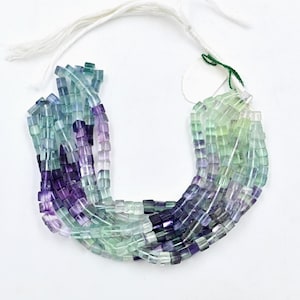 May include: A strand of square-shaped fluorite beads in shades of green, blue, and purple. The beads are strung on a white cord.