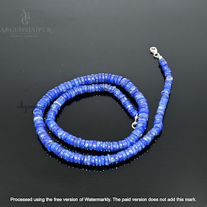 May include: A necklace composed of small, flat, circular lapis lazuli beads in a deep blue hue. The strand features a silver-toned metal lobster claw clasp at one end. The text ABGEMSJAIPUR GEMS & JEWELRY is visible in the upper left corner.