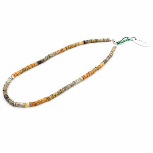 Pode incluir: Um colar composto por pequenas contas redondas e planas em tons de laranja, cinza, preto e branco. As contas são enfiadas para formar uma forma circular. O colar é exibido em um fundo branco.