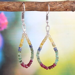May include: A pair of teardrop-shaped earrings with a rainbow of colors. The earrings are made of small, faceted beads in shades of yellow, green, blue, and red. The ear wires and connecting hardware are silver-colored.