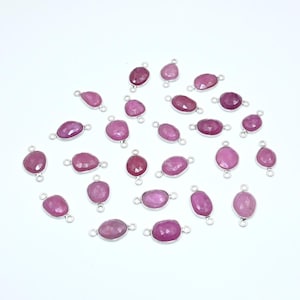 Pode incluir: Uma coleção de 20 pingentes de pedra preciosa rosa com argolas de salto prateadas. Os pingentes são de forma oval e têm um acabamento facetado.