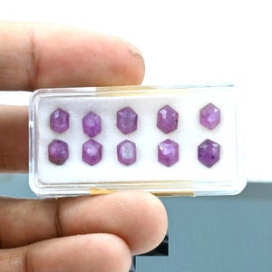 May include: A close-up of a small plastic box containing eight faceted purple gemstones. The gemstones are arranged in two rows of four.