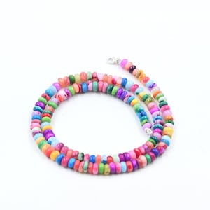 May include: A colorful beaded necklace featuring a variety of vibrant colors including pink, blue, green, and yellow. The necklace is made of small, round beads and has a silver clasp. The beads are approximately 0.25 inches in diameter.