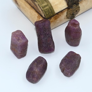 Könnte beinhalten: Fünf rohe, ungeschliffene, violette Rubingesteine. Die Edelsteine haben verschiedene Formen und Größen.
