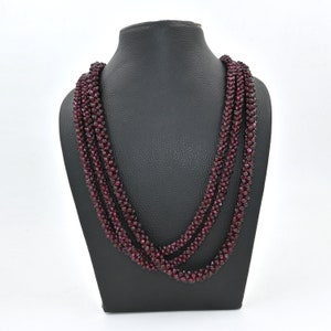 May include: A multi-strand necklace made of small, dark red garnet beads. The necklace is displayed on a black mannequin bust.