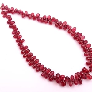 May include: A strand of deep red gemstone beads in a teardrop shape. The beads are strung on a thin cord and are ready to be used for jewelry making.