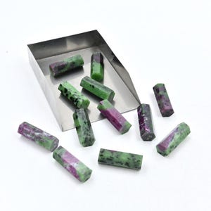 Może przedstawiać: Kolekcja zielonych i fioletowych surowych kamieni szlachetnych w metalowej tacy. Surowe kamienie mają kształt długich, prostokątnych pryzmatów.