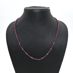 May include: A delicate necklace composed of small, faceted beads. The necklace features a gradient of colors, with ruby red beads transitioning to emerald green. The necklace is displayed on a black mannequin, showcasing its design.