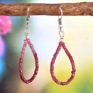 May include: A pair of dangle earrings with a teardrop shape made of pink gemstone beads. The earrings are silver and have a hook closure.
